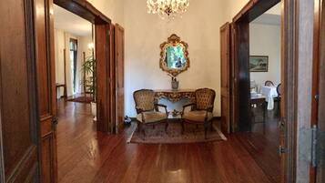 A hallway with a wooden floor, a chandelier, a mirror, and two chairs.