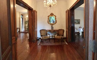 A hallway with a wooden floor, a chandelier, a mirror, and two chairs.
