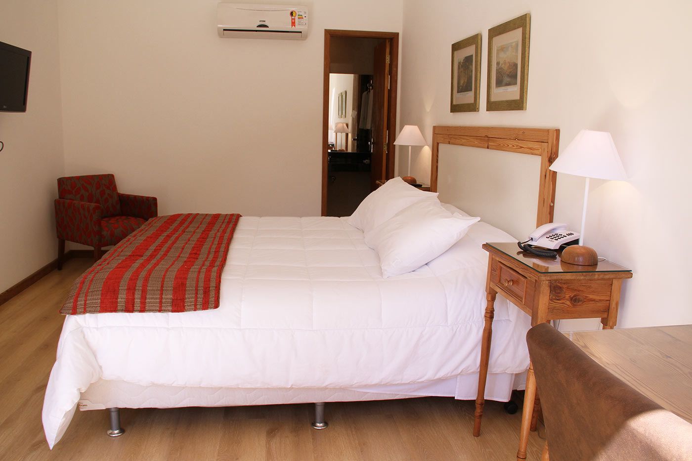 A neatly arranged bedroom with a bed, bedside table, chair, and an air conditioning unit on the wall.