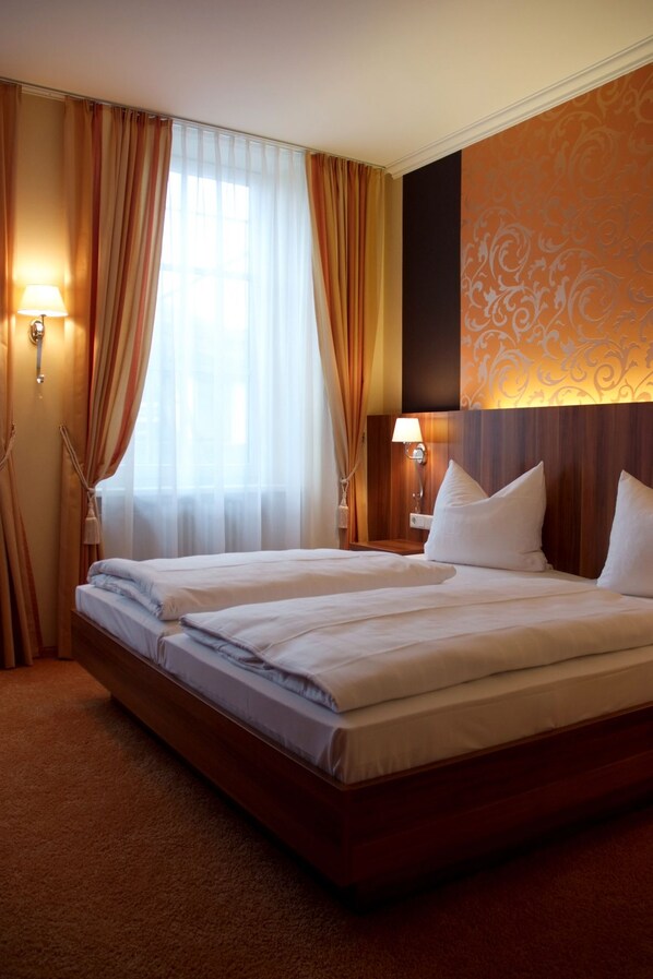 A hotel room with two beds, a large window with curtains, a wall with a decorative pattern, and two wall-mounted lamps. - Dagstuhler Hof (Wadern)