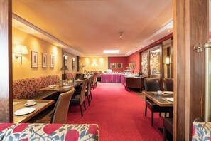 A restaurant with booths and tables, red carpet, and wall-mounted lamps. - Dagstuhler Hof (Wadern)