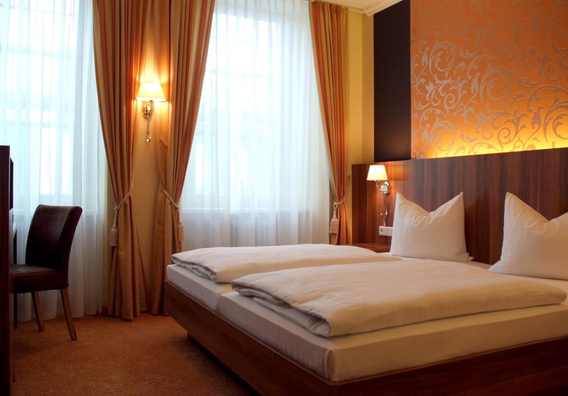 A hotel room with two beds, a chair, and a wall-mounted lamp.