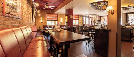 A restaurant with leather booths, a long wooden table, and a bar area.