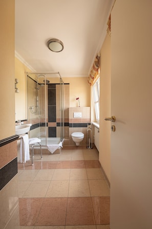 A bathroom with a glass shower enclosure, a toilet, a sink, and a window with curtains. - Dagstuhler Hof (Wadern)