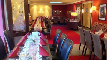 A hotel dining area with a long table set for a meal, multiple chairs, and a red carpet.