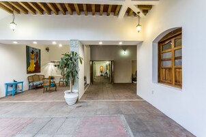 Un amplio espacio interior con piso de baldosas, una planta grande en maceta y una ventana con marco de madera.