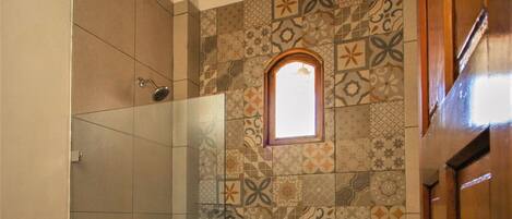 A bathroom with a shower, a toilet, and a patterned wall.