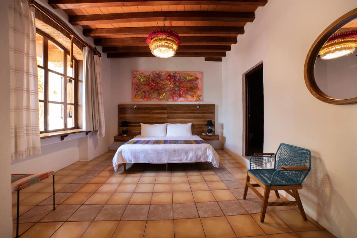 Un dormitorio con cabecera de madera, cama con colcha a rayas, una silla, un cuadro en la pared y una araña.