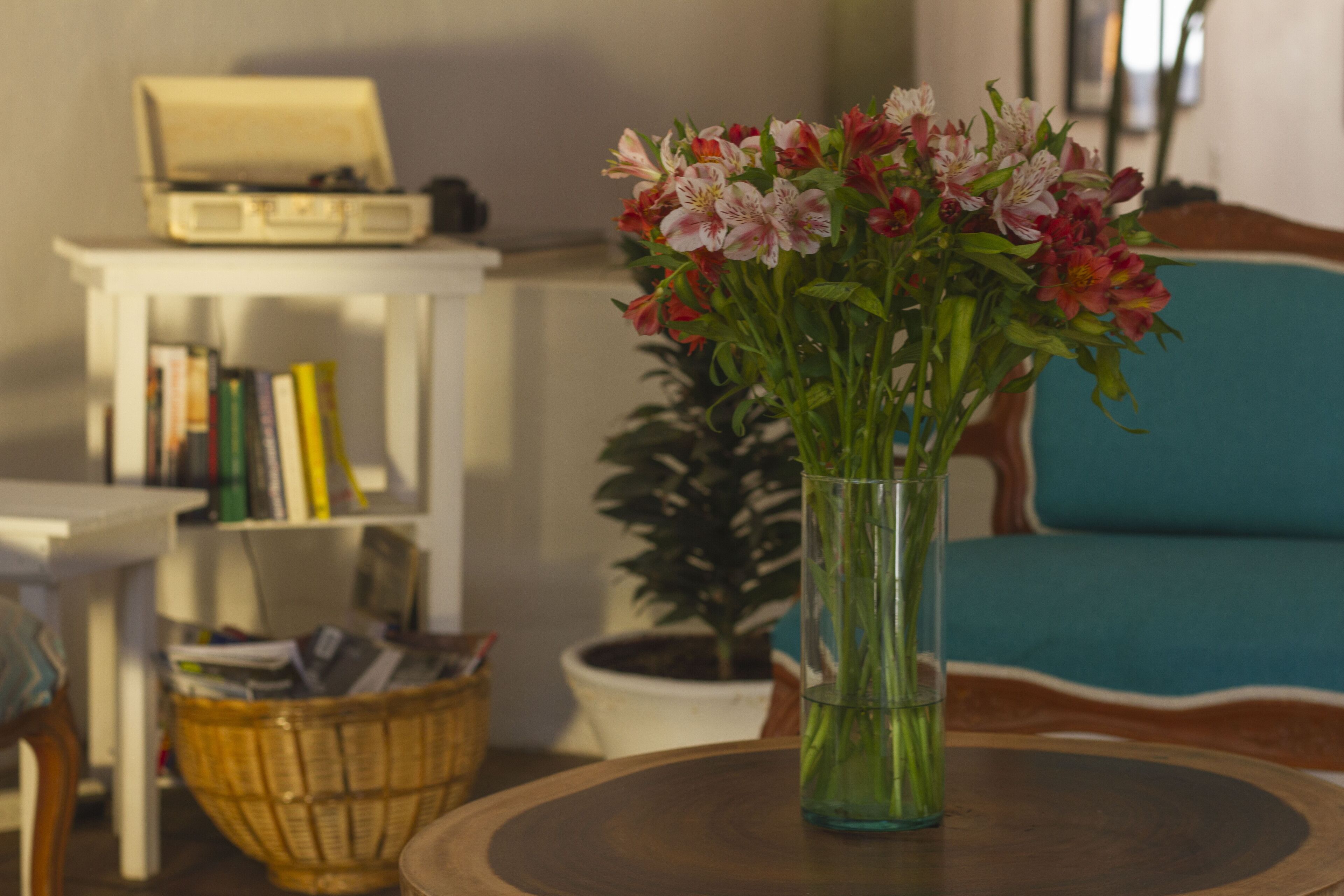 A room with a wooden table, a vase with flowers, a bookshelf, and a blue sofa.