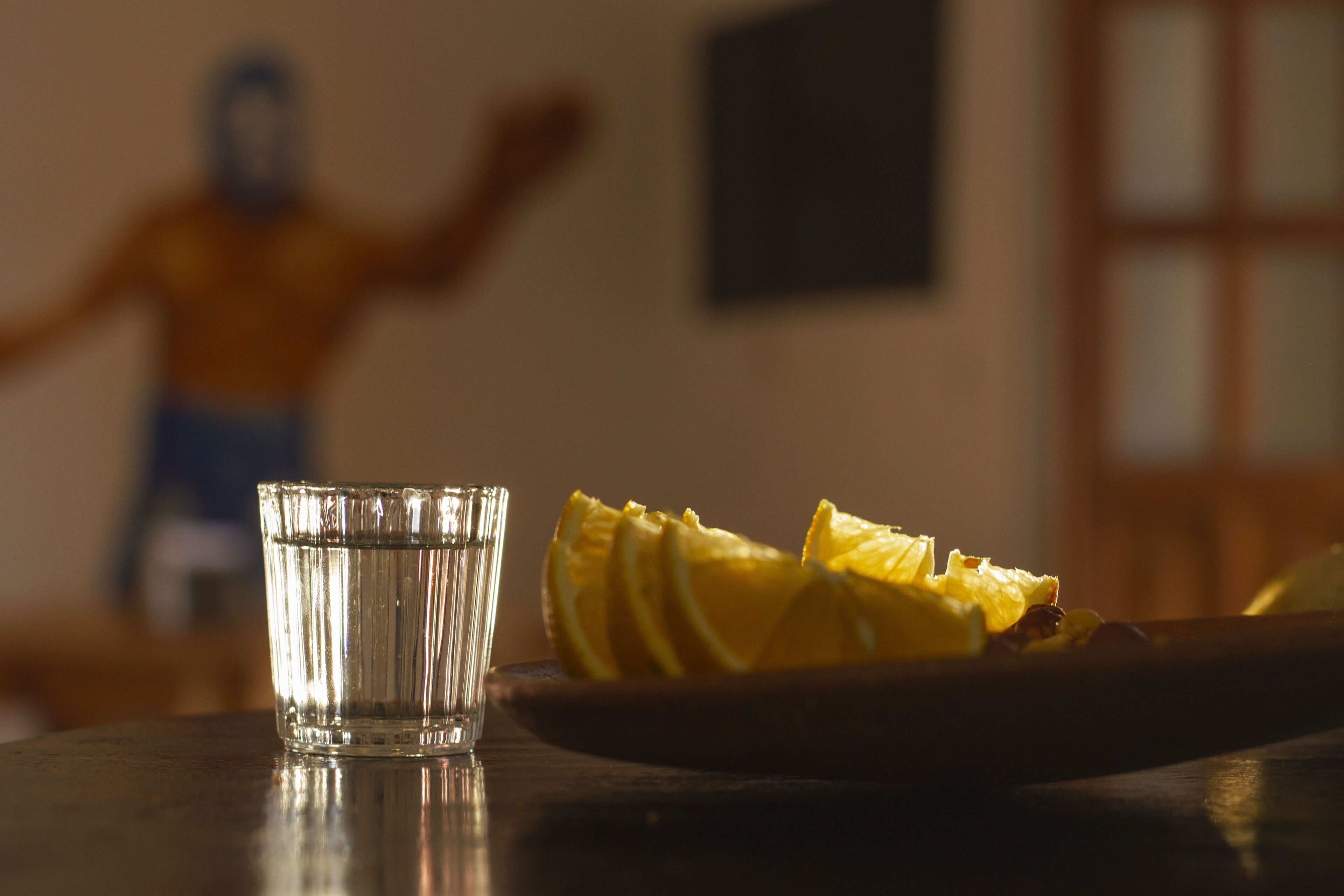A glass of water and a plate with sliced fruit on a table.