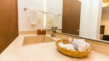 Un baño con lavamanos, espejo y una cesta de artículos de aseo.