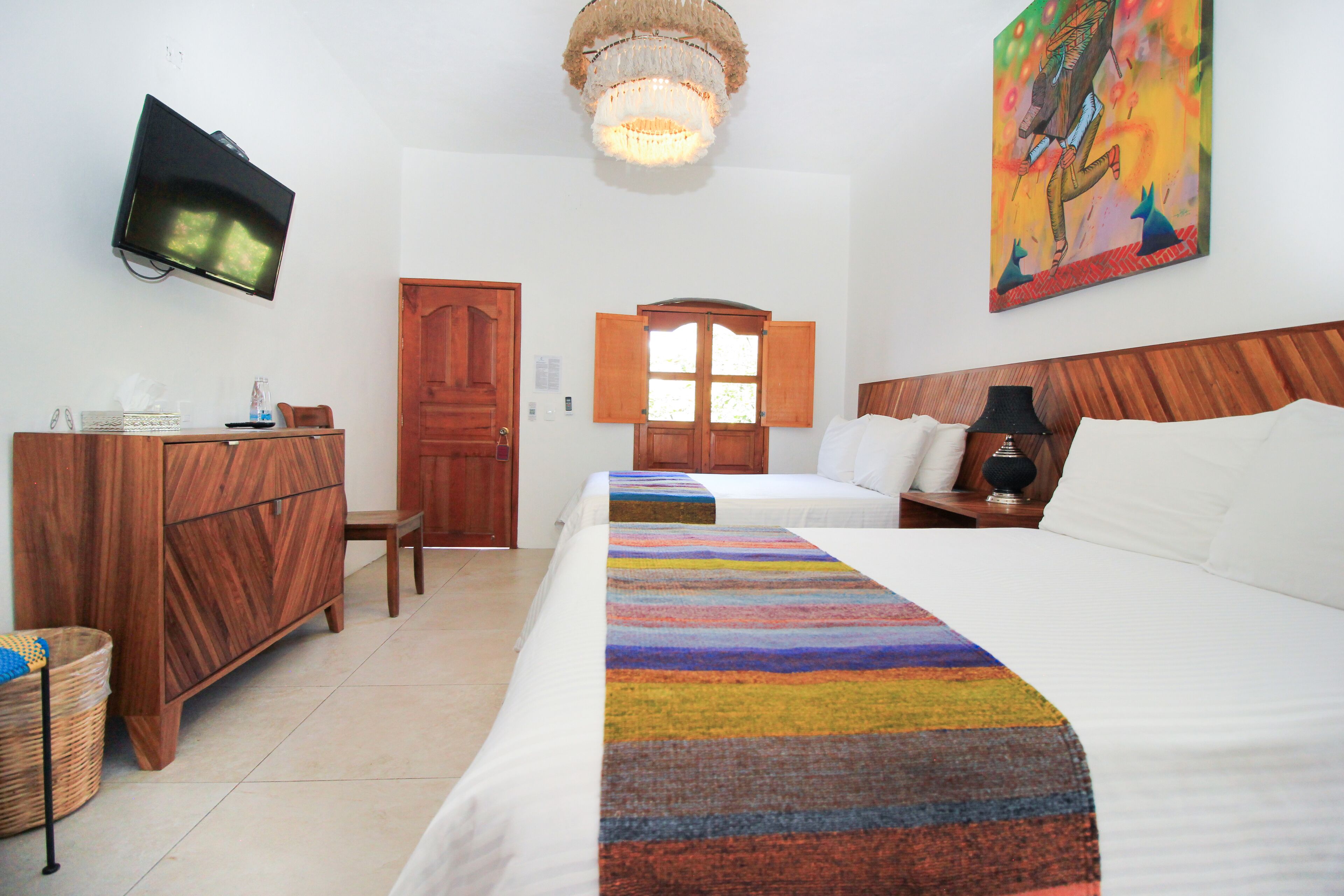 Una habitación de hotel con cama, escritorio, televisor, un cuadro y una araña.
