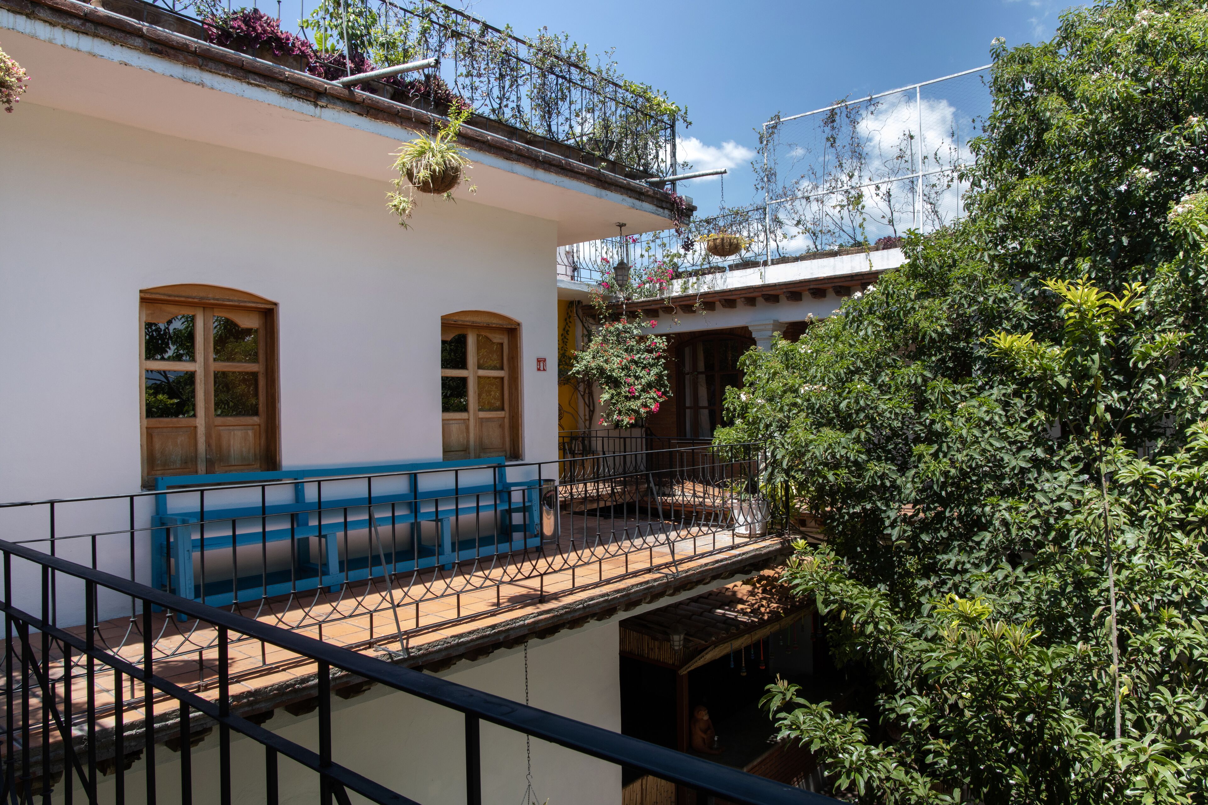 A building with a balcony, a blue bench, and hanging plants.