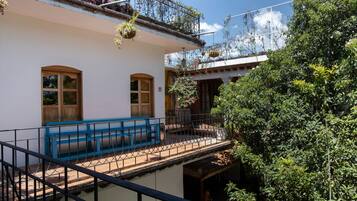 Un bâtiment doté d’un balcon, d’un banc bleu et de plantes suspendues.