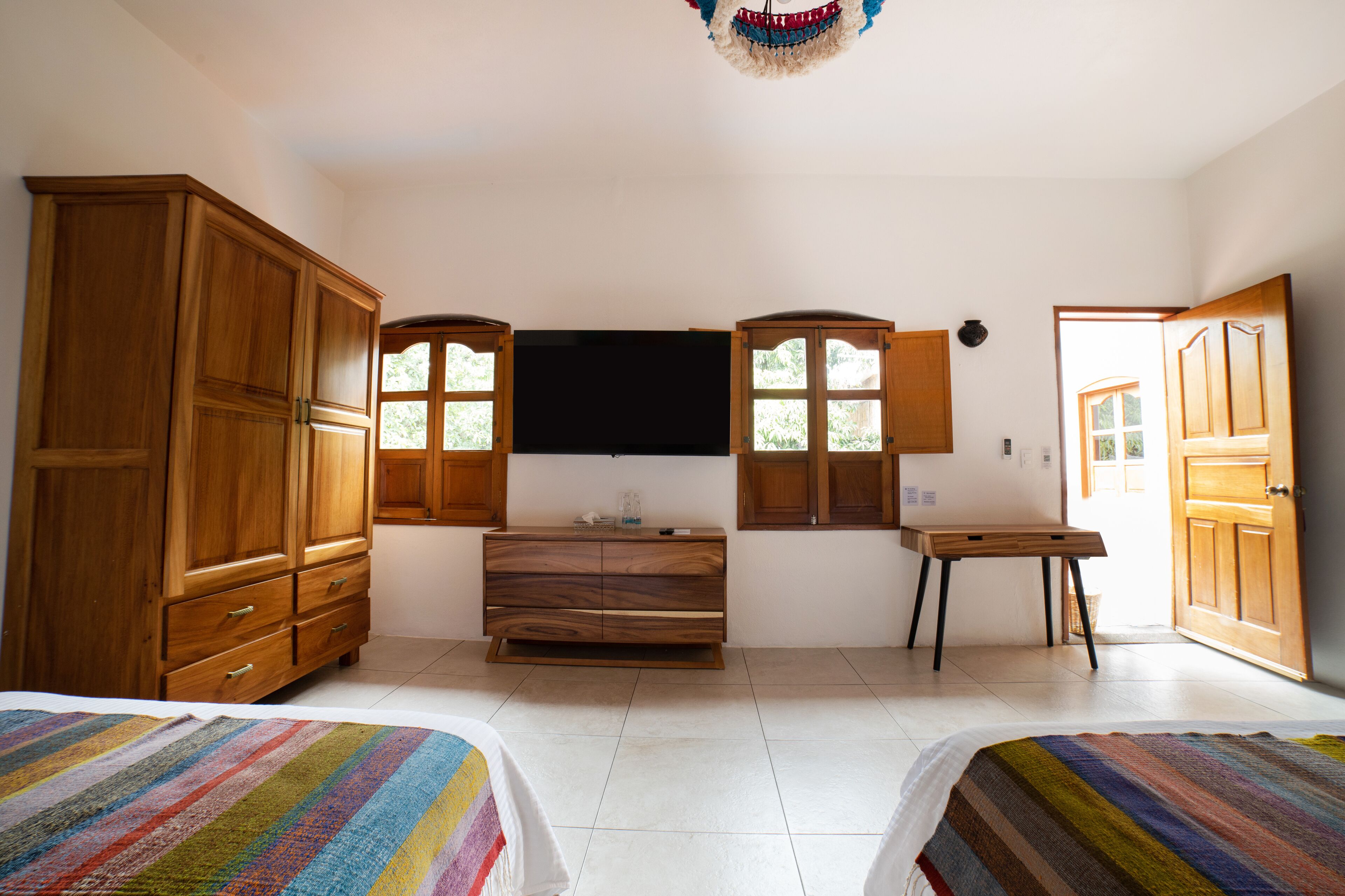 A bedroom with two beds, wooden furniture, a flat-screen TV, and a window.