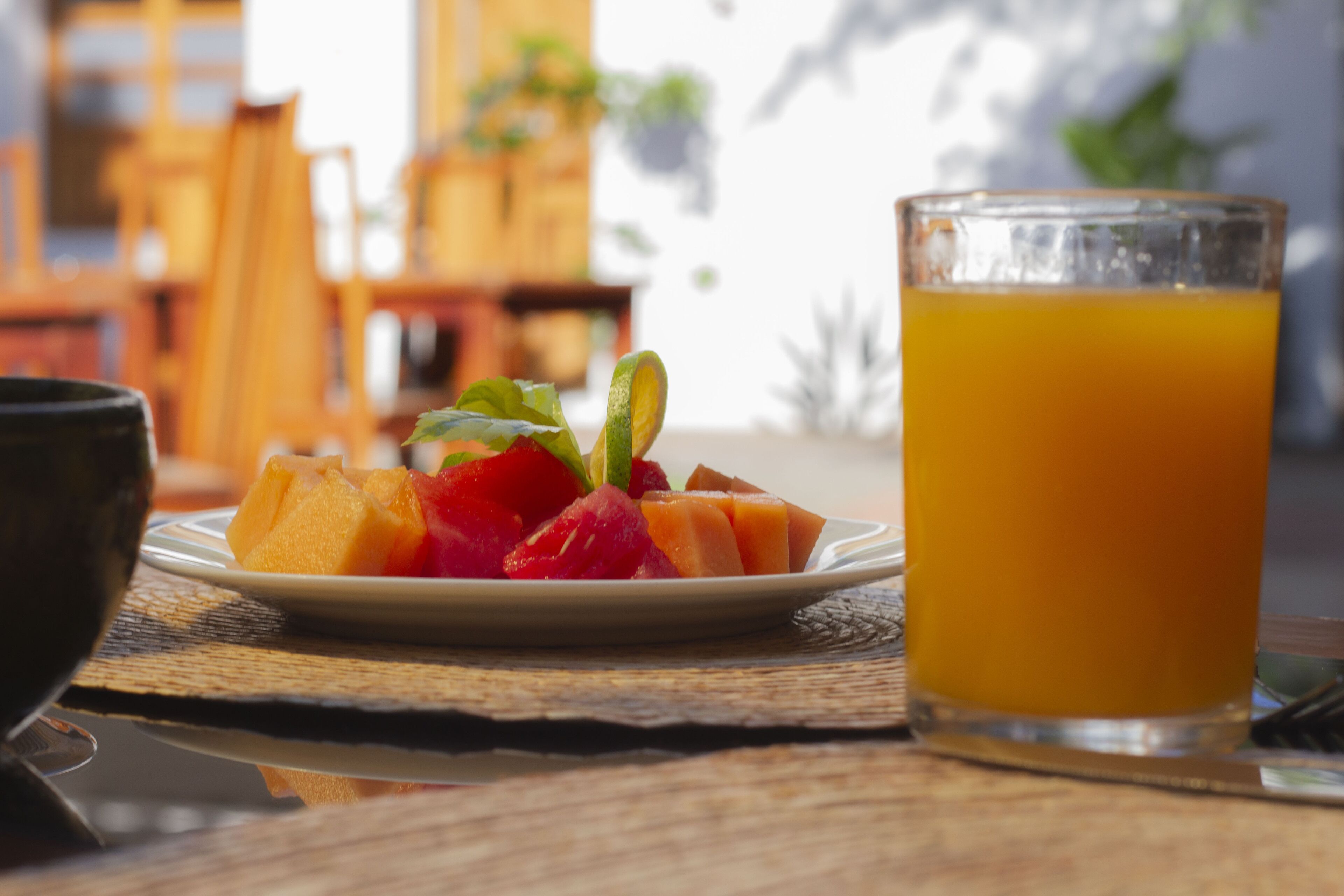 Een bord fruit en een glas sinaasappelsap op een houten tafel.