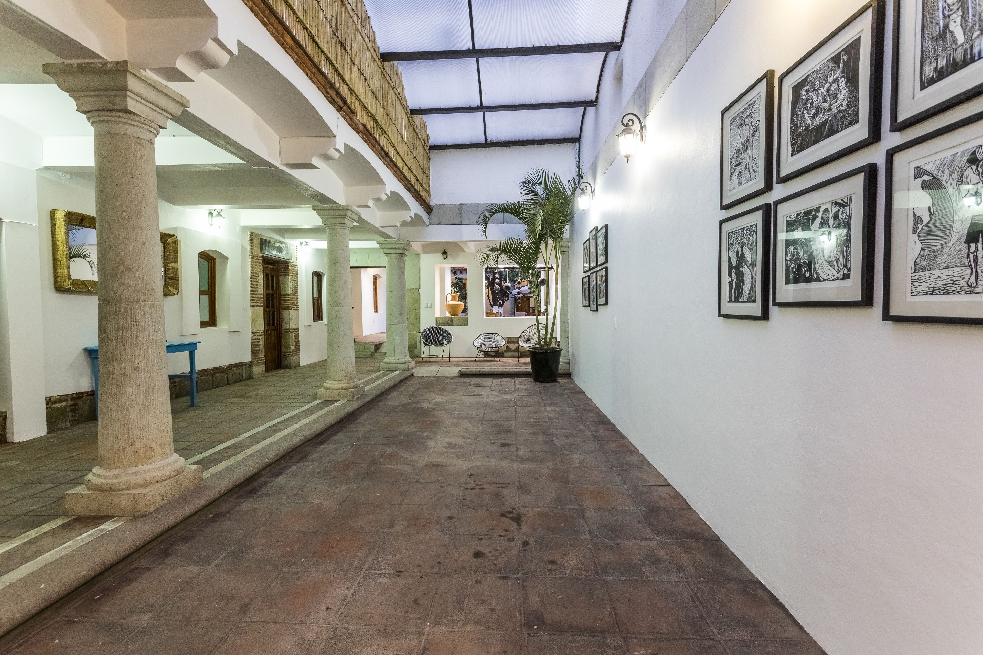 A corridor with columns, a tiled floor, and framed artwork on the walls.