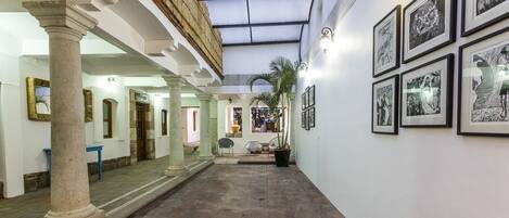 A corridor with columns, a tiled floor, and framed artwork on the walls.