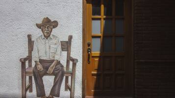 Un mural que muestra a un hombre sentado con sombrero, en una pared junto a una puerta de madera con paneles de vidrio.