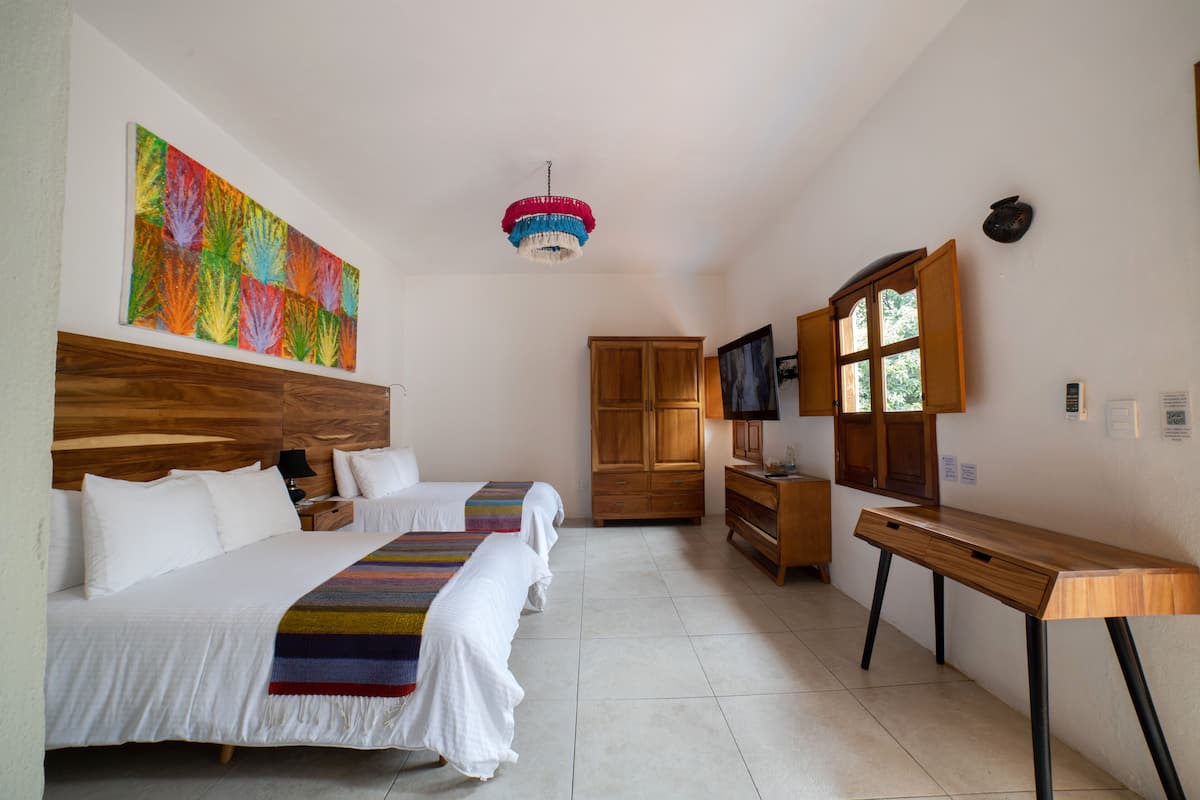 Habitación de hotel con dos camas, cabecero de madera, una obra de arte colorida, televisor y escritorio.
