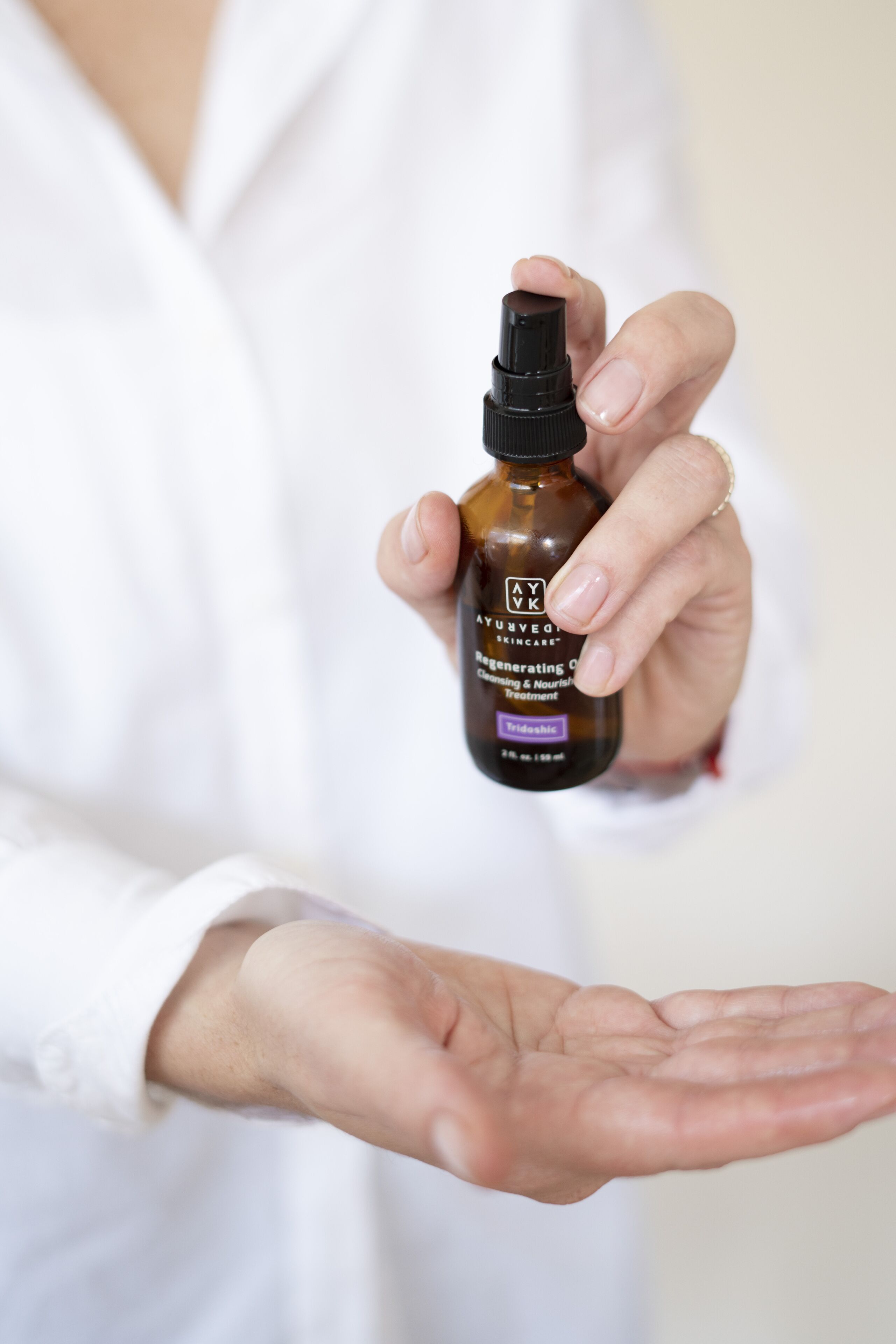 Una persona sosteniendo una botella etiquetada como "AYURVEDO SKINCARE" con un gotero.
