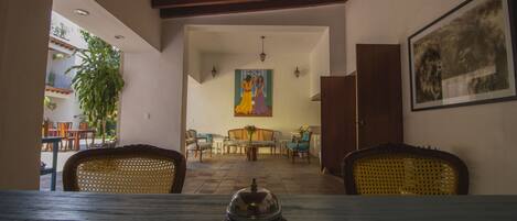 A dining area with a table set for two, a wooden ceiling, and a painting on the wall.