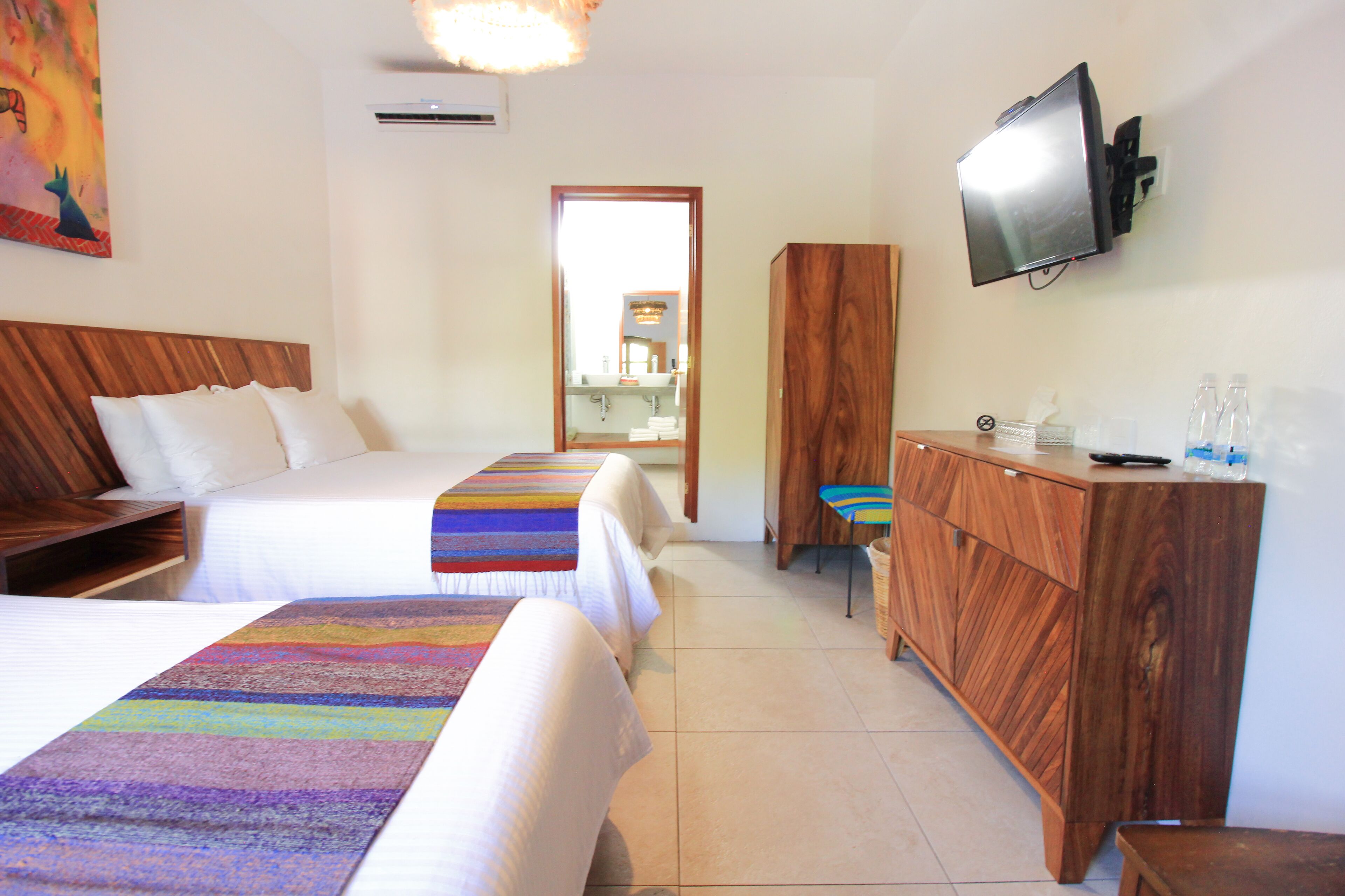 A hotel room with two beds, a wooden dresser, a television, and a bathroom visible through an open door.
