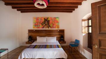 Ein Schlafzimmer mit einem Holz-Kopfteil, einem farbenfrohen Gemälde über dem Bett, einem blauen Sessel und einer Holztür.