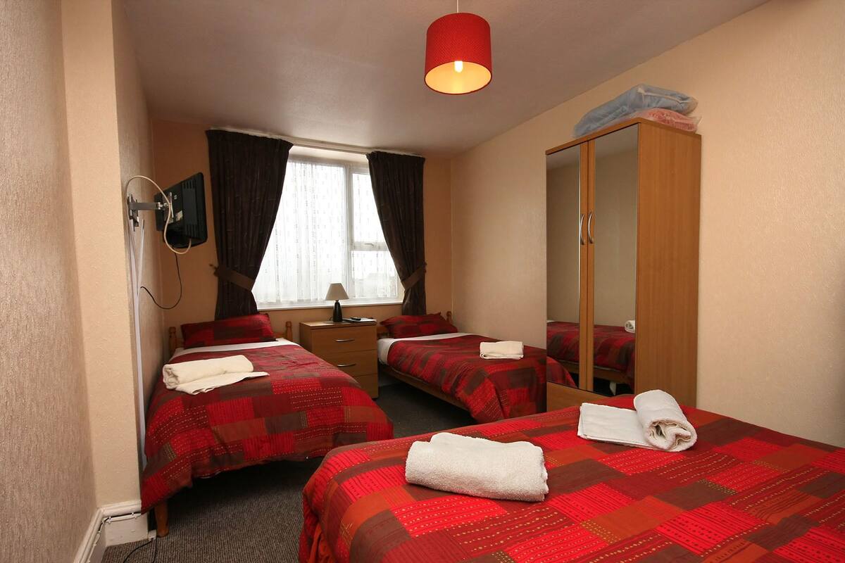 A hotel room with two beds, a wooden wardrobe, a desk, a chair, a television, and a window with curtains.