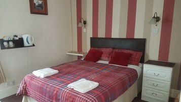 Een hotelkamer met een bed, nachtkastje, een plank met toiletartikelen en een wandlamp.
