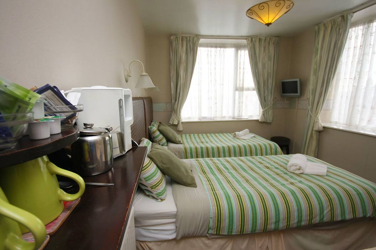 A hotel room with two beds, a desk with a kettle and a lamp, and a television on the wall.
