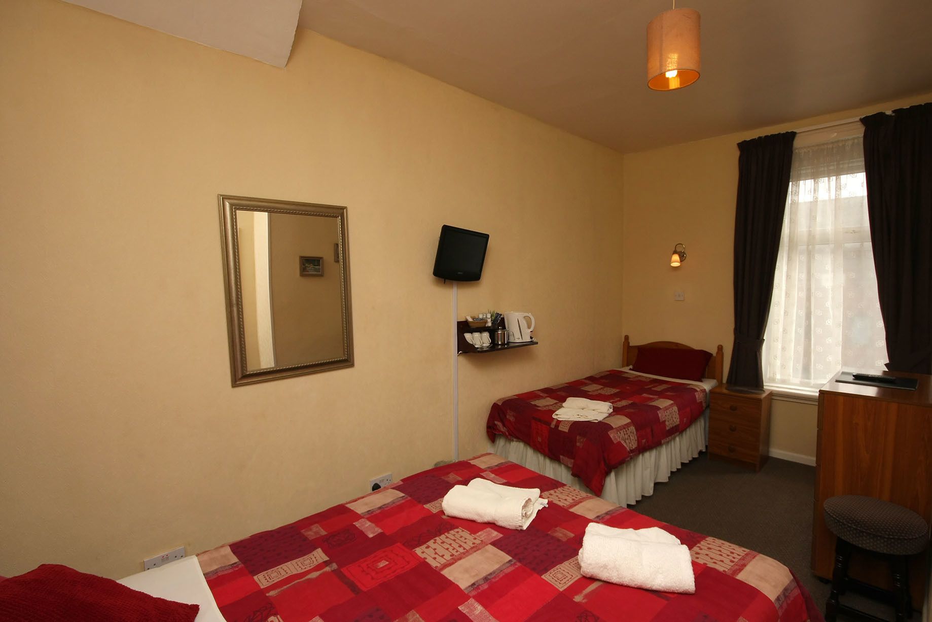 A hotel room with two beds, a television, a small table with a lamp, and a window with curtains.