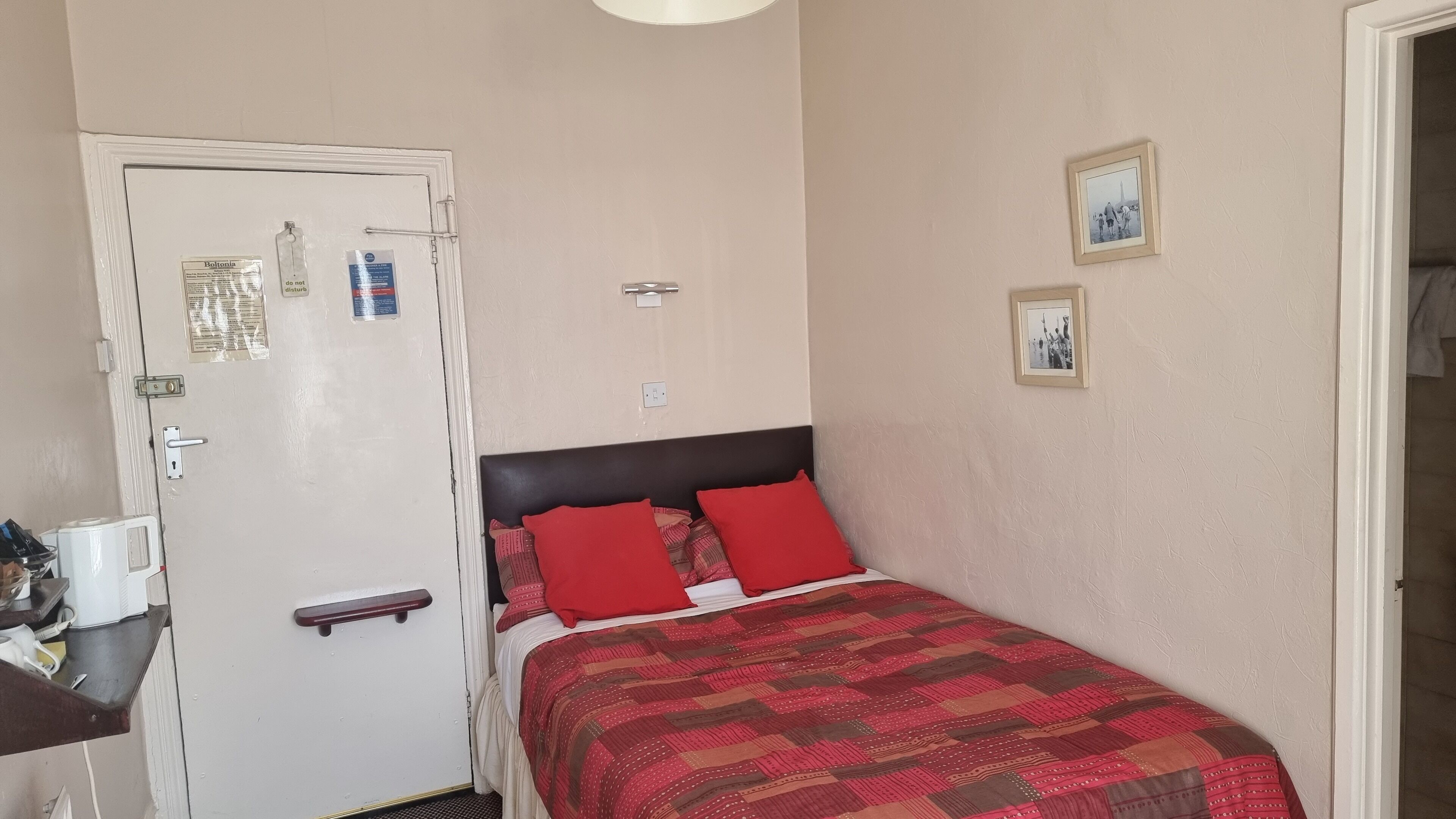 A bedroom with a bed, a door with a bulletin board, and a small table with a telephone.