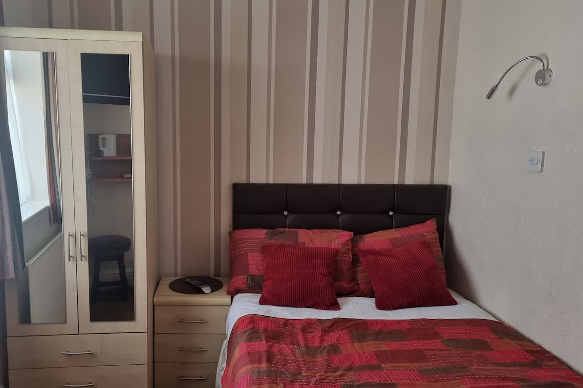 A bedroom with a bed, a wardrobe, a bedside table, and a window with curtains.