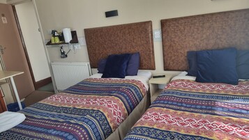 Een hotelkamer met twee bedden, elk voorzien van beddengoed met een patroon, een nachtkastje met een afstandsbediening en een wandplank met toiletartikelen.