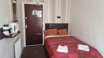 Een kleine hotelkamer met een enkel bed, een nachtkastje met een waterkoker, een spiegel en een deur met een bericht.