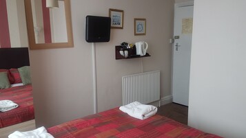 Een hotelkamer met een bed, een radiator, een plank met toiletartikelen en een deur met een bordje.