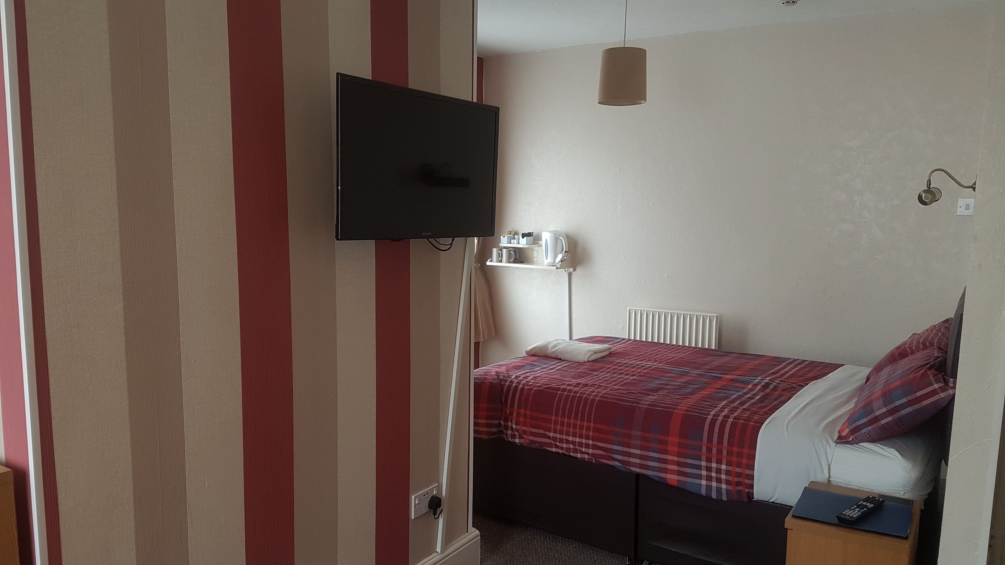 A bedroom with a bed, a television mounted on the wall, a bedside table, and a radiator.