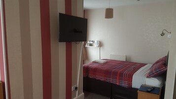 A bedroom with a bed, a television mounted on the wall, a bedside table, and a radiator.