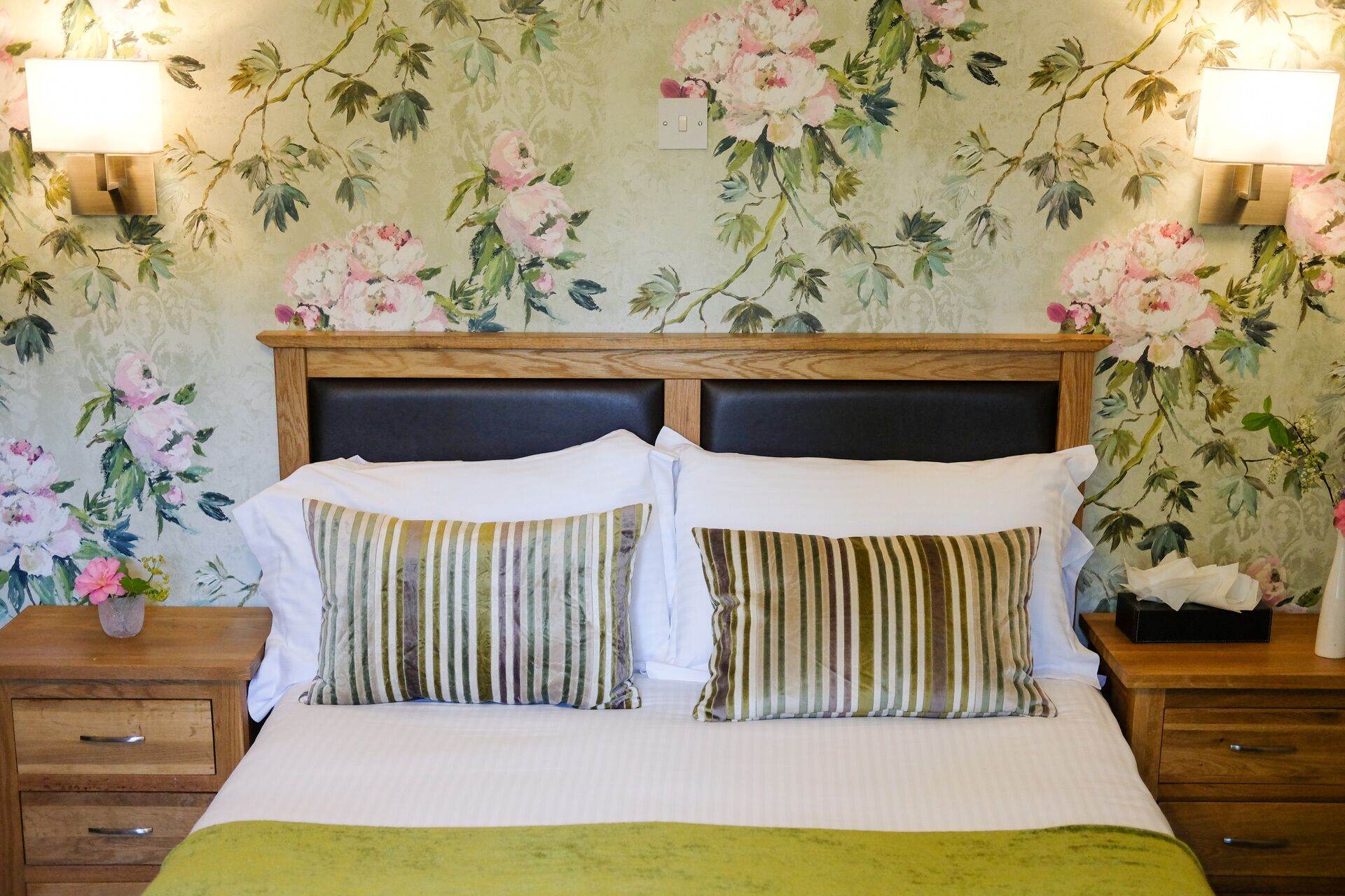 A double bed with striped pillows, a wooden headboard, and a nightstand with a lamp.