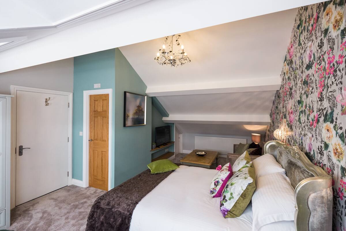 A bedroom with a large bed, a television, a small table, and a door.