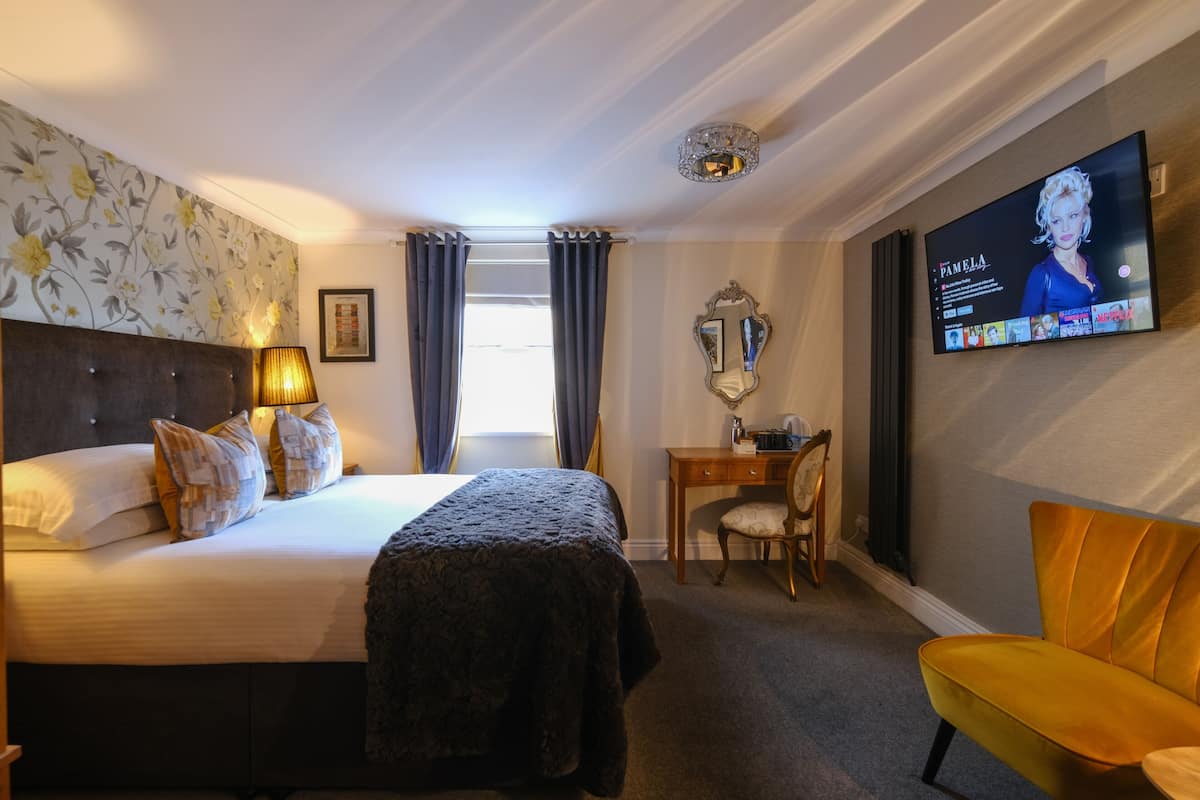 A hotel room with a bed, a desk, a chair, a television, and a window with curtains.