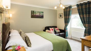 Une chambre à coucher avec un lit, une table de chevet en bois, un plaid vert, un vase avec des fleurs, un tableau représentant une forêt, un canapé en cuir noir, des rideaux à carreaux et une fenêtre donnant sur un paysage.