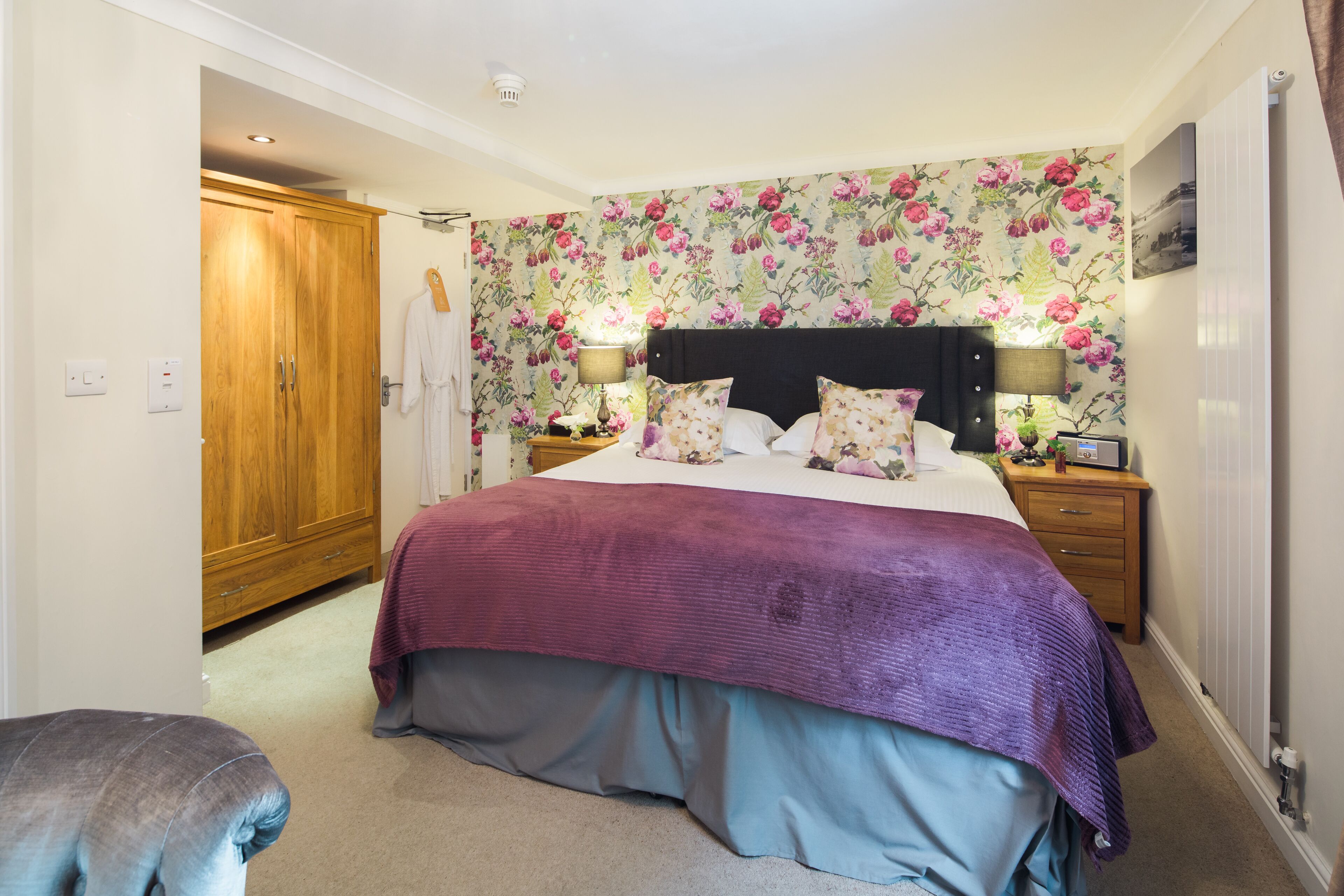 A bedroom with a bed, nightstands, a wooden wardrobe, and a floral wallpaper.