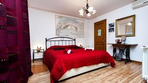 Ein Schlafzimmer mit einem Bett, Holzboden, roter Bettdecke, einem Bild an der Wand, einem Spiegel und einer Heizung.