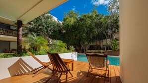 A wooden deck with two wooden chairs and a table, overlooking a swimming pool and lush greenery. - Private pool Access 2BR condo in the best location in Tulum (Tulum)