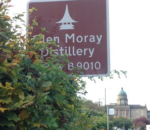 A sign for the Glen Moray Distillery with a building in the background.