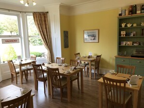 A dining area with wooden tables and chairs, a green cabinet with kitchenware, and a 'VACANCIES' sign on the window.