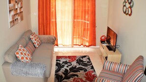 Un salon avec un canapé, un tapis à motifs, un téléviseur et des rideaux orange.