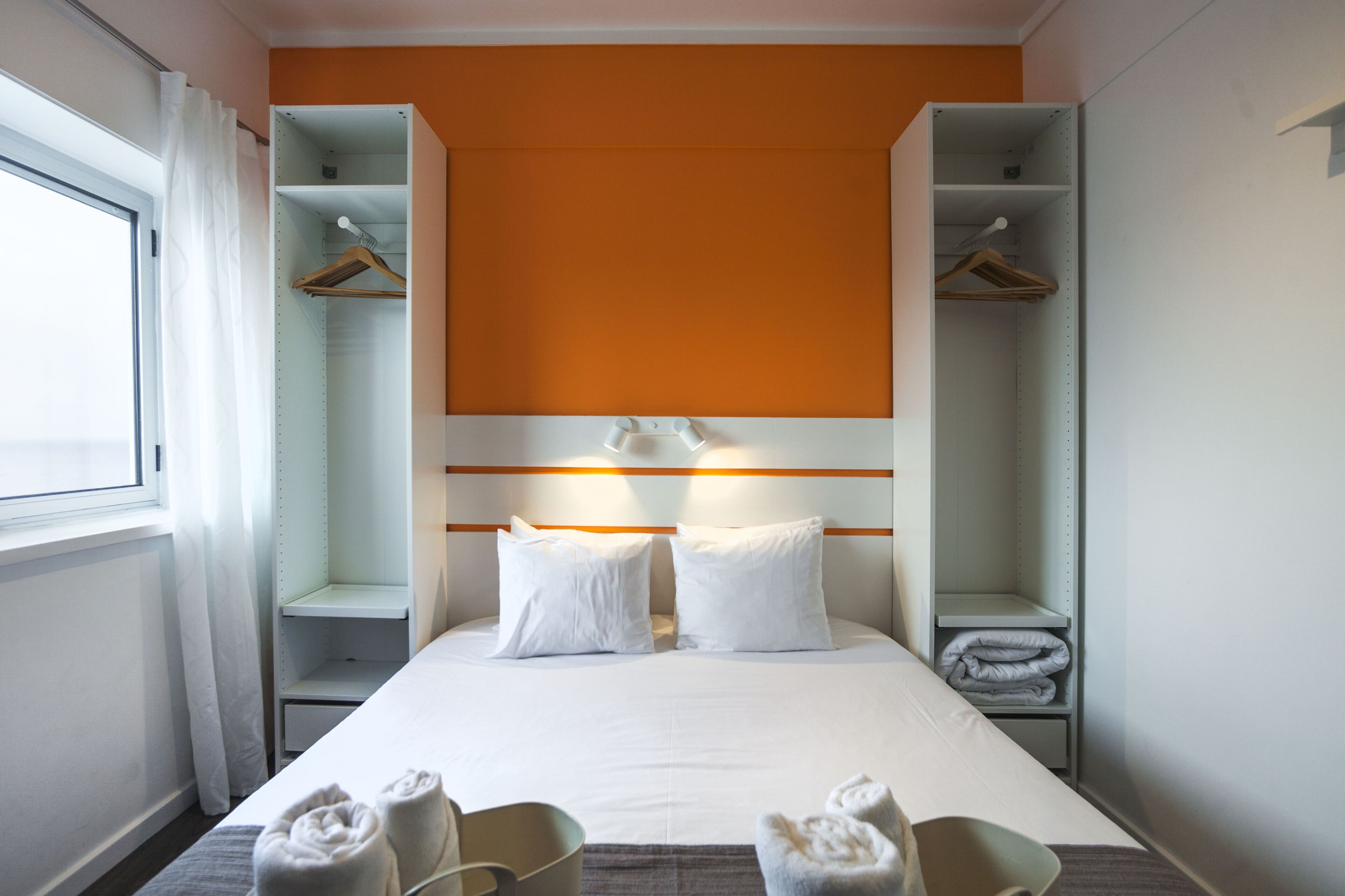 Una habitación de hotel con cama, dos mesitas de noche, un armario y una ventana con cortinas.